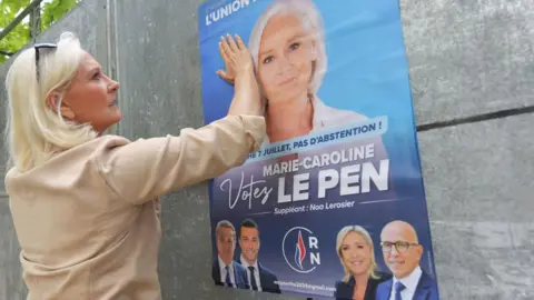 JEAN-FRANCOIS MONIER/AFP  French far-right National Rally (RN) party member and candidate for the second round of legislative elections Marie-Caroline Le Pen, puts her hand on a campaign poster in Brains-Sur-Gée, western France