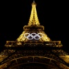 A view of the Olympic rings beneath the Eiffel Tower, lit up at night.