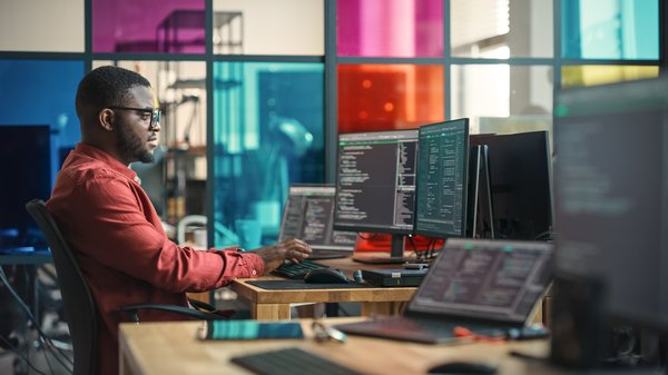 A coder at a workstation in front of several computer screens.