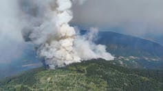 Wildfire smoke is seen rising above a hill top.