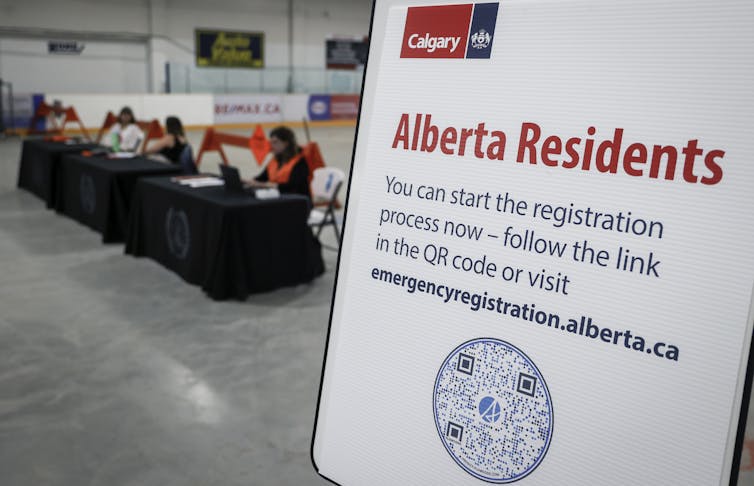 A row of people are sat at a table with a sign in the foreground.