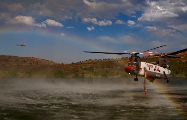 A CH-47D Chinook helicopter ripples the water with its rotor blades, creating a rainbow as it reloads with water at Green Ridge Glade Reservoir, while another helicopter passes in the background to help fight the Alexander Mountain fire west of Loveland on Tuesday, July 30, 2024. (Photo by Zachary Spindler-Krage/The Denver Post)