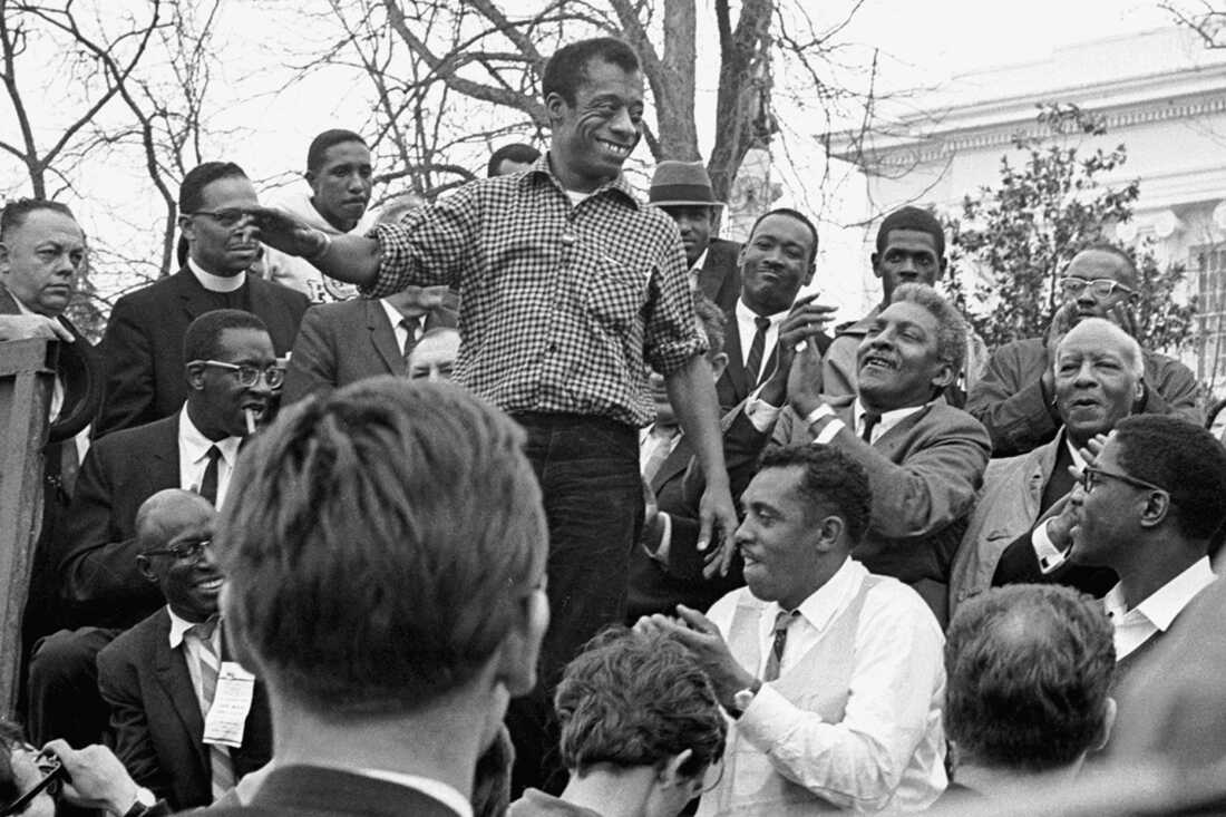 James Baldwin smiles while addressing the crowd from the speaker's platform, after participating in the march from Selma to Montgomery in support of voting rights, Alabama, March 1965.