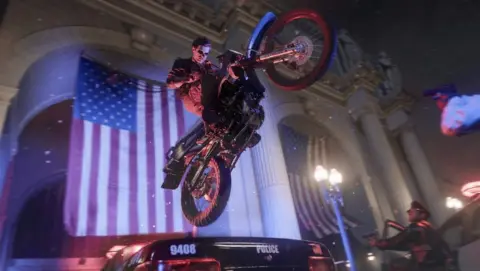 Activision A screenshot from a video game shows a man riding a motorcycle in the air jumping over a police car in front of a building with an American flag on it