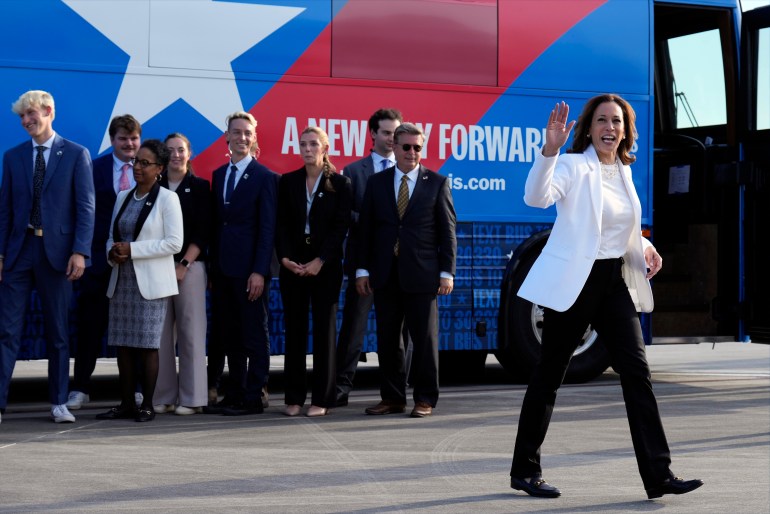 Kamala Harris disembarks a branded campaign bus, surrounded by staffers and supporters.