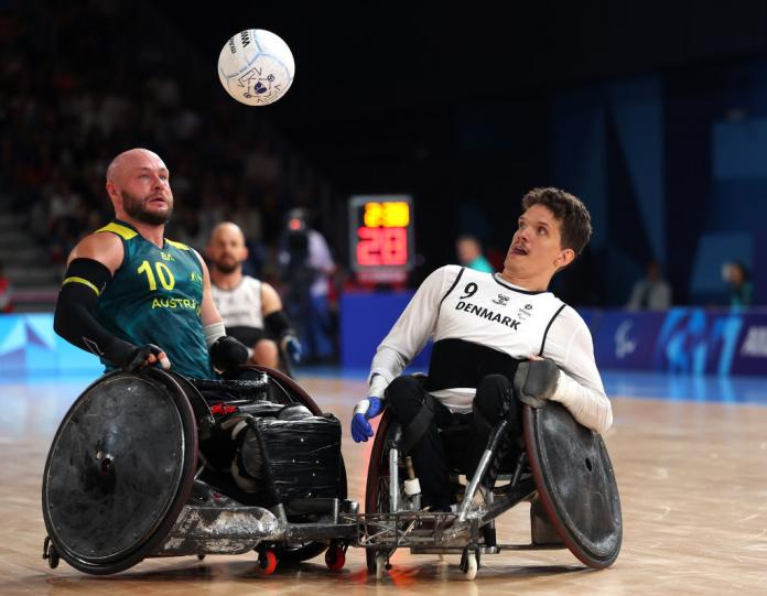 Two wheelchair rugby players, one in green and one in white, compete for the ball at Paris 2024