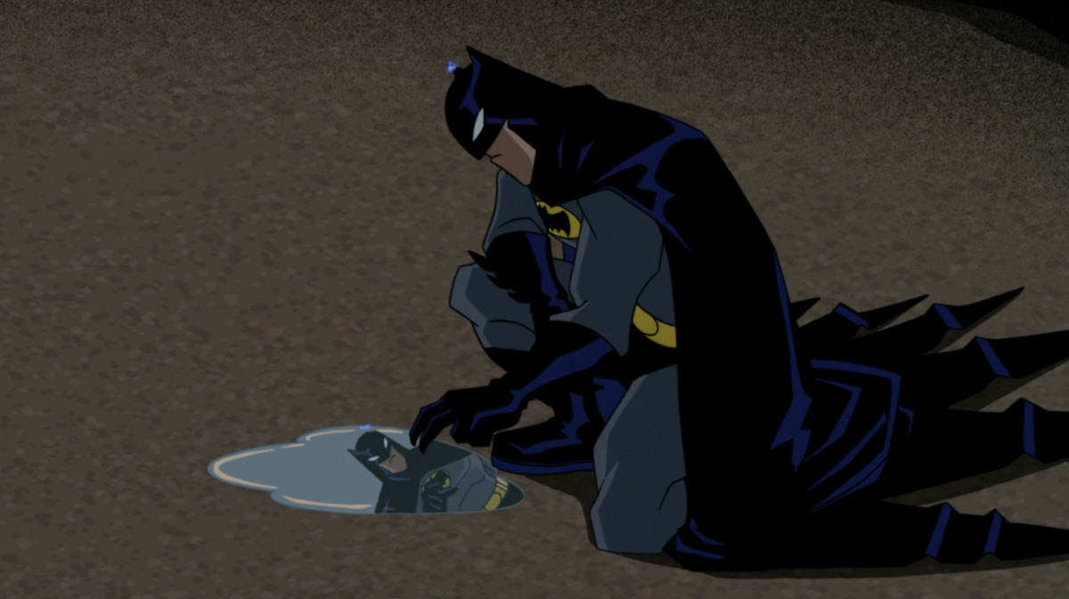 Batman looking at himself in a puddle on the ground in a still from The Batman (2004)