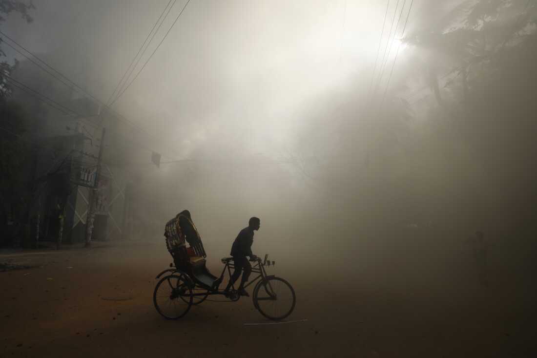 A rickshaw puller rides in the smoke caused by a burning shopping center that was set on fire by protesters during a rally against Prime Minister Sheikh Hasina and her government in Dhaka, Bangladesh, on Sunday.