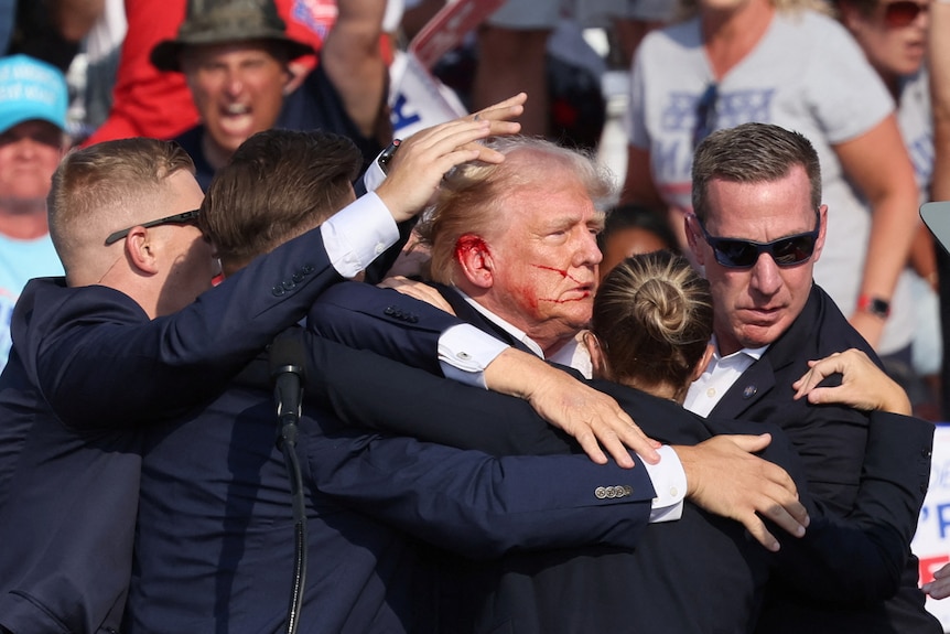 Donald Trump is shielded by secret service as blood spreads from an injury on his ear 