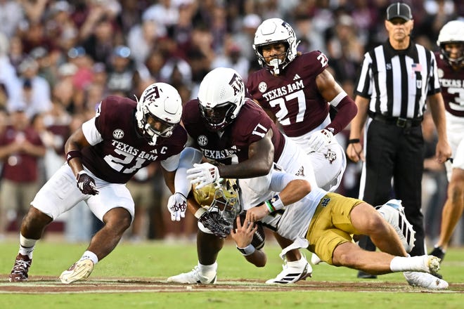 Texas A&M Aggies linebacker Taurean York (21) and defensive lineman Albert Regis (17) tackle Notre Dame Fighting Irish quarterback Riley Leonard (13) during the second quarter Aug. 31, 2024 at Kyle Field in College Station.