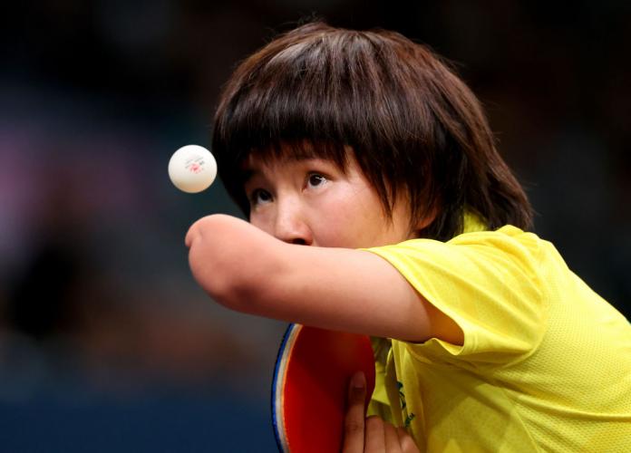 A woman throws a table tennis ball in the air and watches it intently