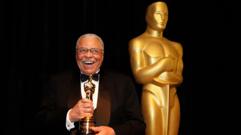 Getty Images Wearing a black and white tuxedo with a black bow tie James Earl Jones smiles clutching his honorary Oscar next to a statue of an Oscar Award. This was taken at the 84th Annual Academy Awards show in Los Angeles in February 2012.