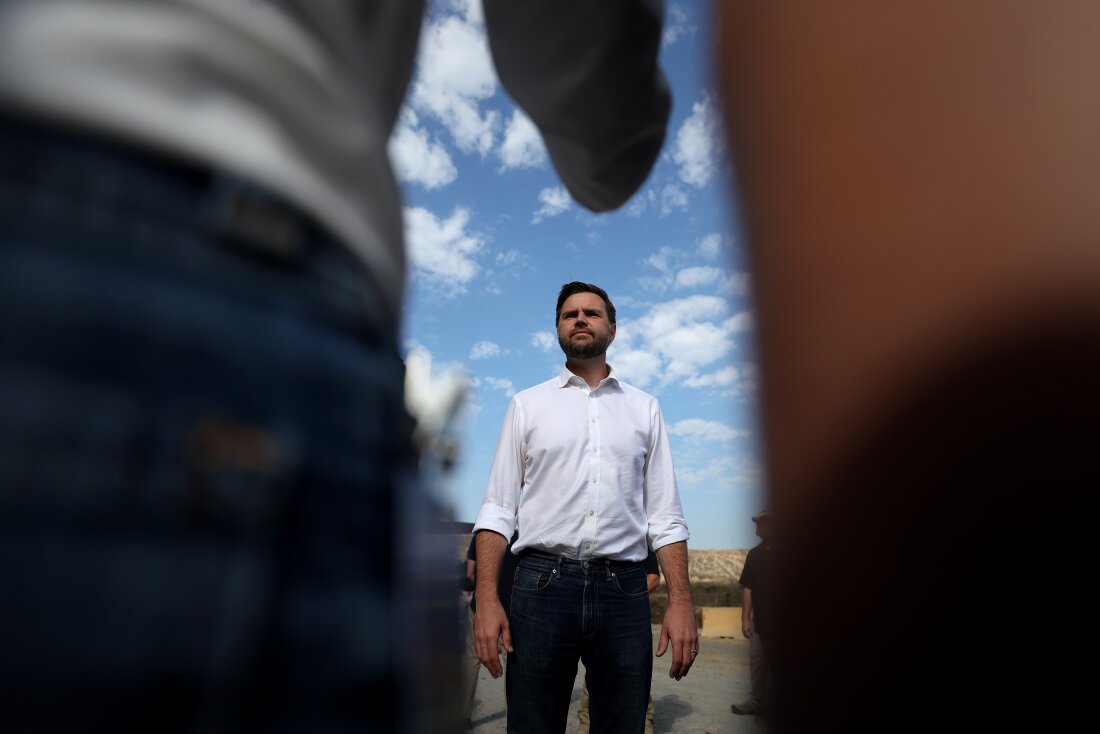 This photo shows Sen. JD Vance of Ohio, the Republican vice presidential nominee, speaking to reporters in front of the border wall with Mexico on Sept. 6 in San Diego. Wearing jeans and a white shirt, he's standing against a blue sky with white clouds.