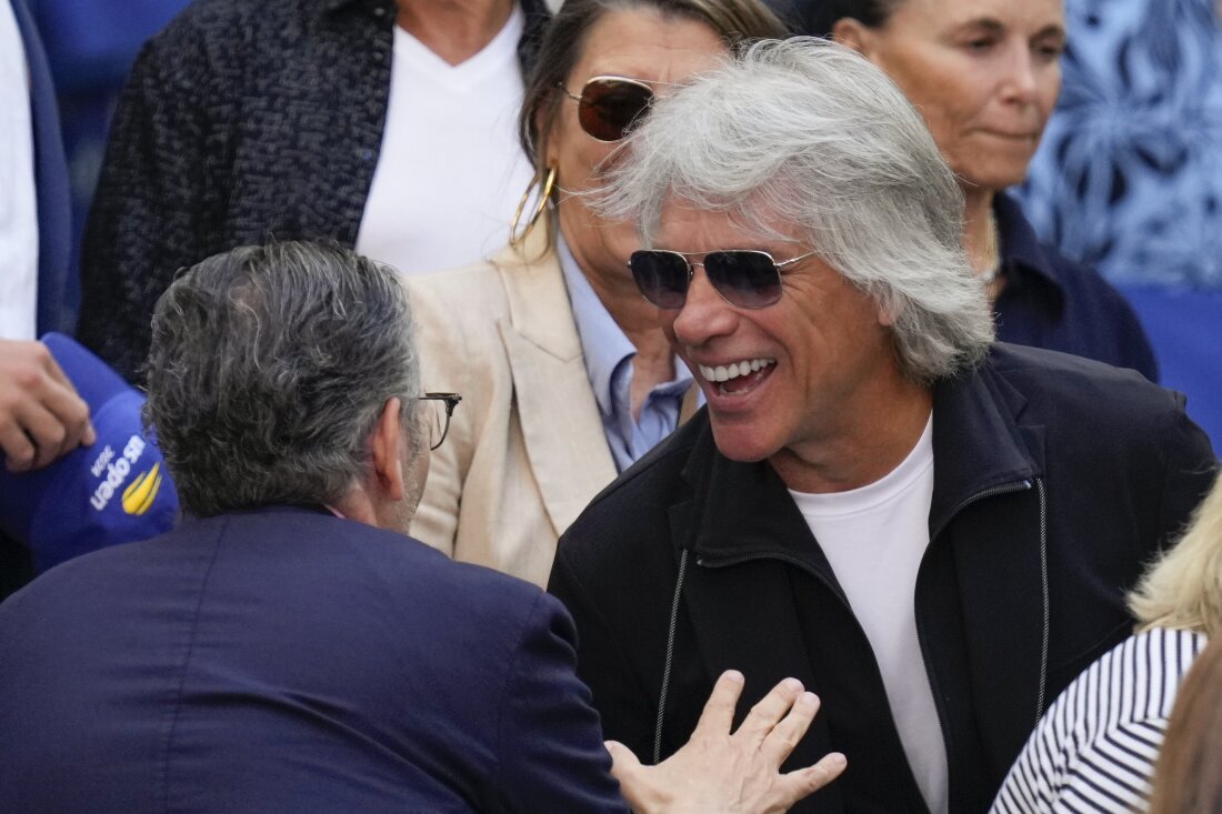 Jon Bon Jovi smiles while speaking to someone in the stands at the U.S. Open tennis championships.