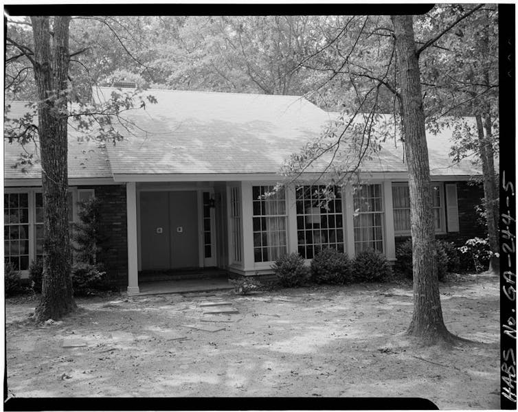 A black and white ranch-style house behind trees.