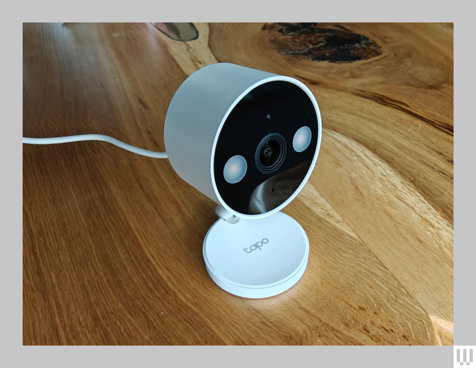 Small white security camera with a discshaped top and small circular base sitting on a wooden surface