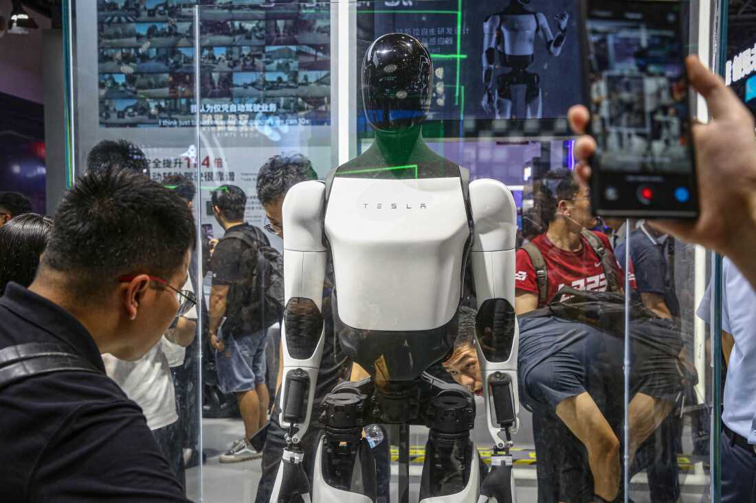 Visitors look at Tesla's humanoid robot Optimus at its exhibition booth during the World Artificial Intelligence Conference (WAIC) in Shanghai on July 5, 2024. Optimus, a featureless humanoid robot, can walk and fold laundry. Musk has argued it could eventually learn to do almost anything a human can do.