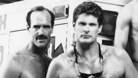 Everett/Shutterstock Michael Newman and David Hasselhoff standing together bare-chested on Baywatch