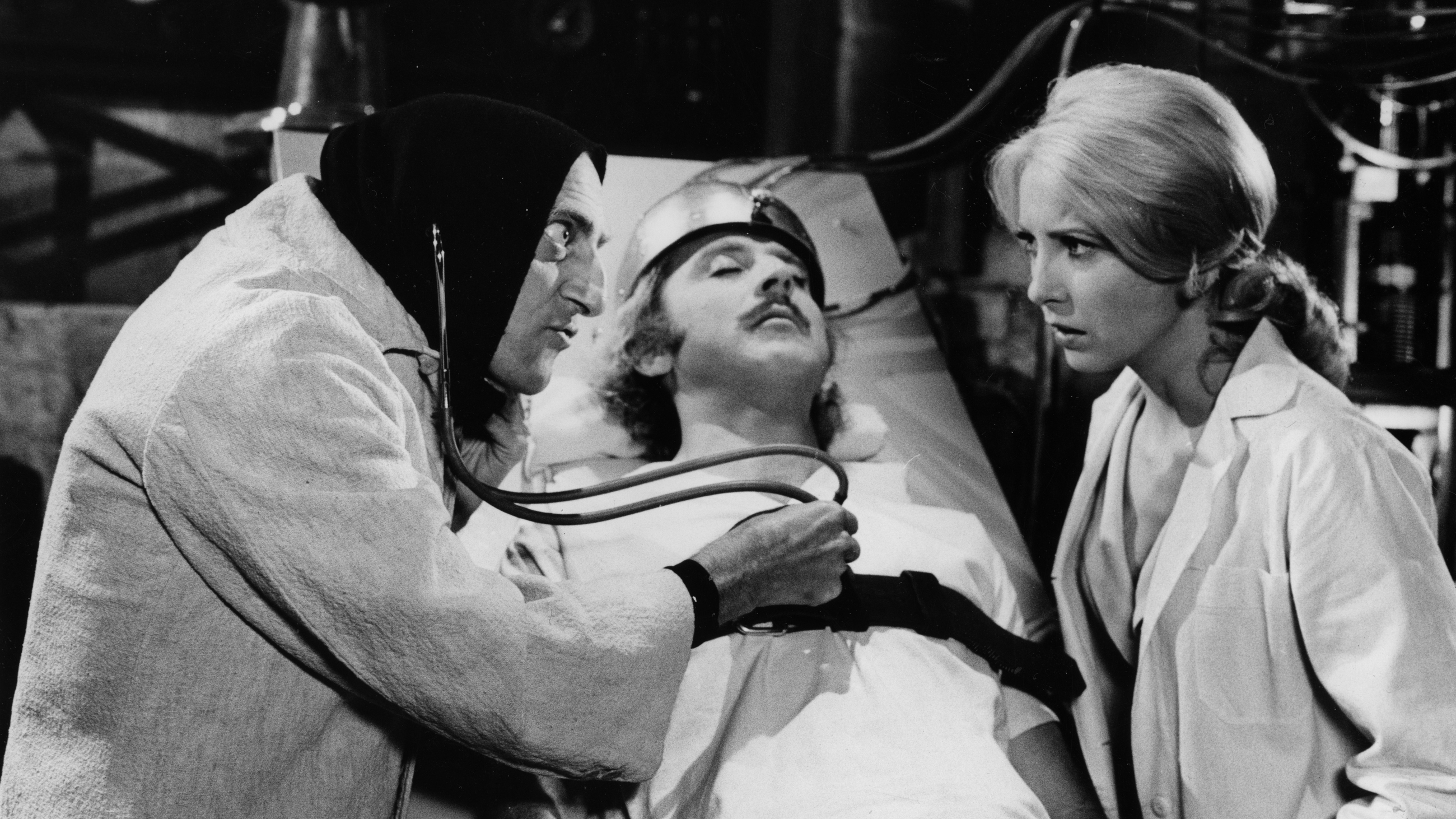 Marty Feldman listens to Gene Wilders' heart as Teri Garr looks on in a scene from the movie Young Frankenstein.