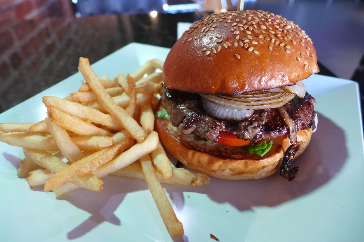 A burger with black stripes on a seeded bun with fries on the same plate.