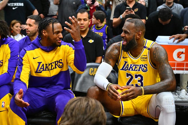 Los Angeles Lakers guard Bronny James (left) talks with his father, LeBron James (23), on the bench during the first half against the Cleveland Cavaliers on Wednesday in Cleveland.