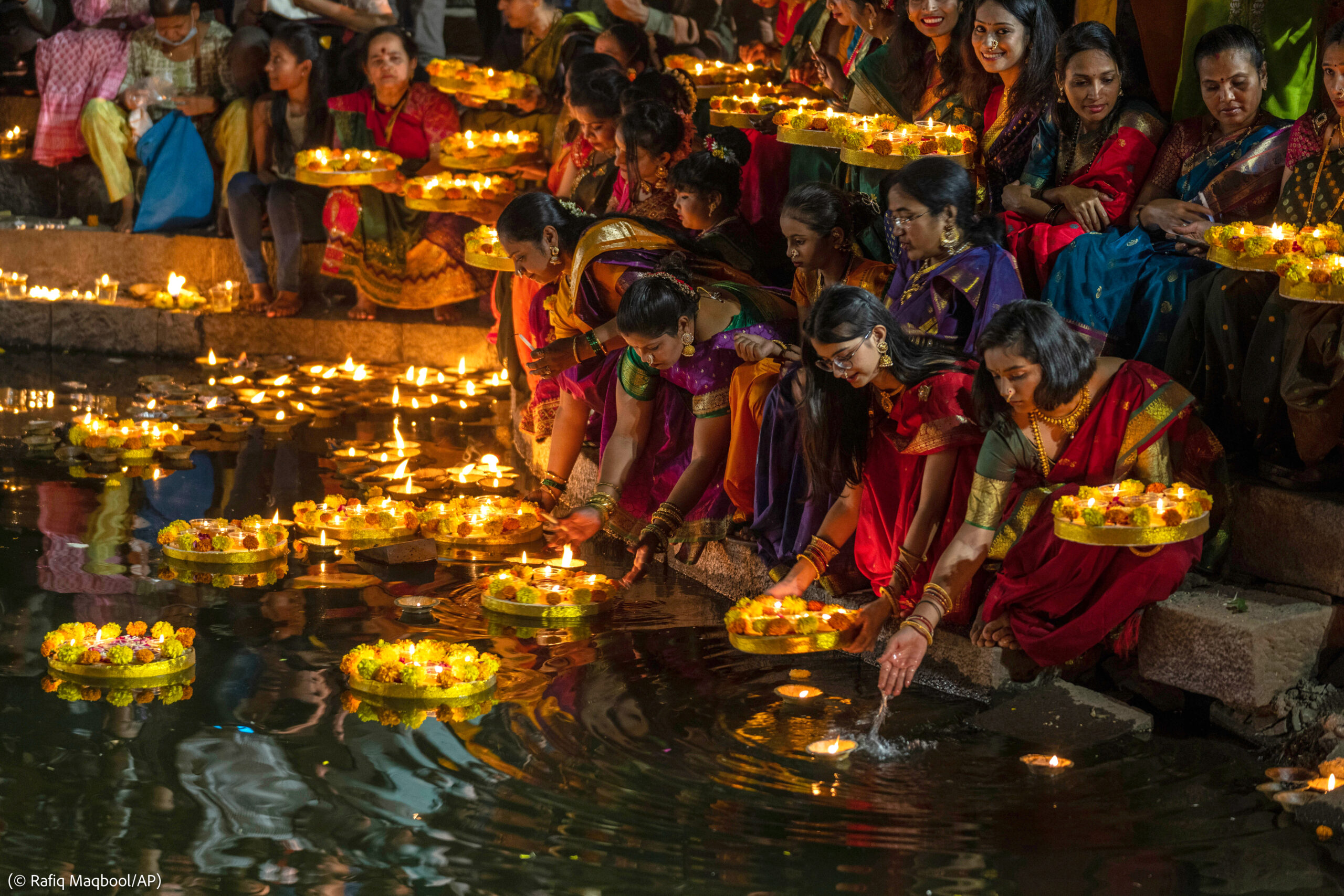 Mujeres vestidas con “saris” encendiendo lámparas de aceite (© Rafiq Maqbool/AP)