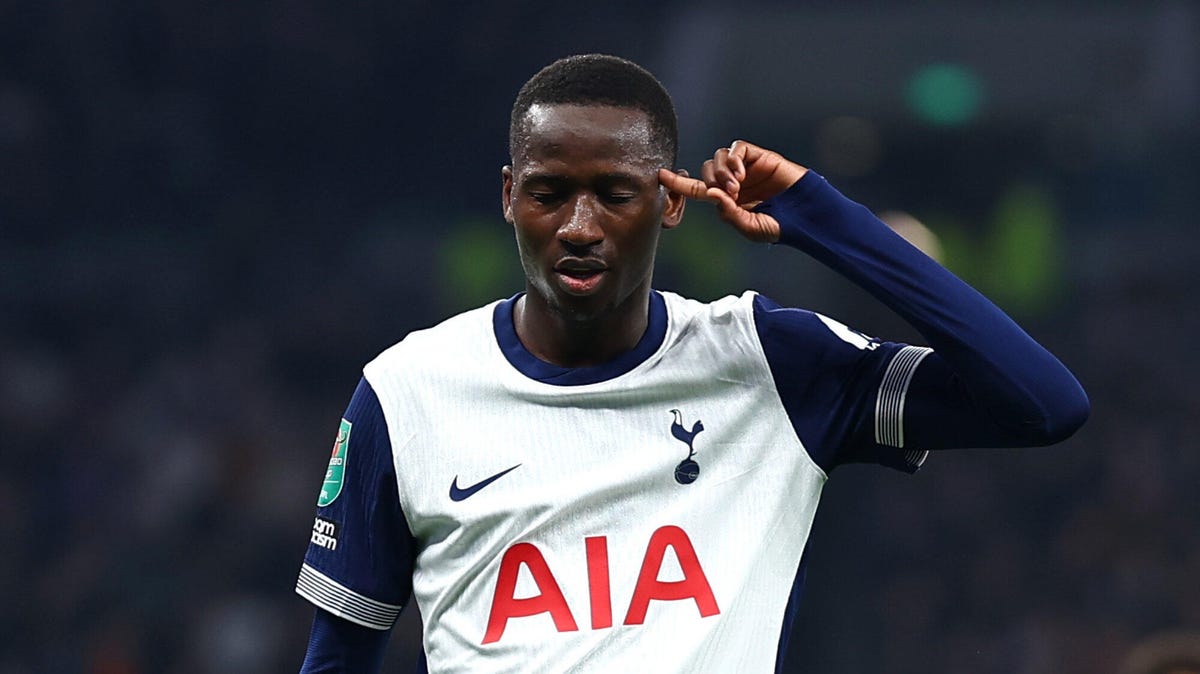 Tottenham Hotspur player Pape Matar Sarr making gesture with his left hand to his head, eyes closed.