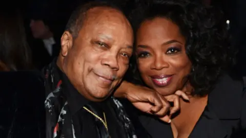 Getty Images Quincy Jones and Oprah Winfrey sitting with their heads close together and smiling at the Rock and Roll Hall of Fame Induction Ceremony in 2013