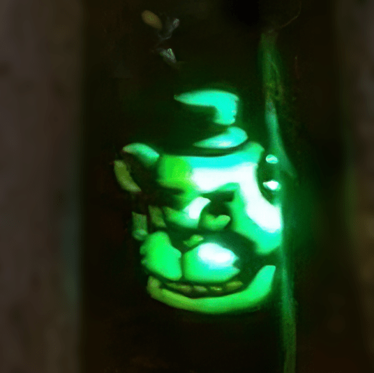 A pumpkin carved with a sinister mascot bear’s face wearing a hat. The bear is lit with a blue-green light.